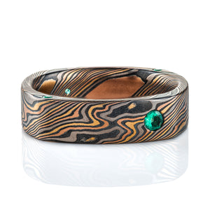 Mokume gane twist patterned ring, with a rounded square shape for the outside of the band, while the inside is still fully rounded and comfort fit to fit the finger well. The outside of the band is flat profiled, with small round emeralds flush set into the corners.