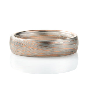 Domed band patterned in mokume style with long thin lines flowing around the ring, made of layers of light and darker gray silver metal, with two layers of red gold added. 