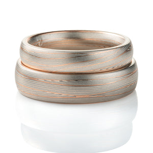 Domed band patterned in mokume style with long thin lines flowing around the ring, made of layers of light and darker gray silver metal, with two layers of red gold added. 