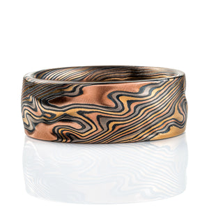 Textured mokume gane band, with carving on the surface to create a rippling effect in relief, similar to rolling hills on a topographic map. Made with layers of red gold, yellow gold, palladium, and silver that has been oxidized to turn it black in color.