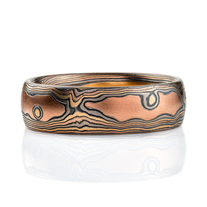 Wide men's style mokume gane band with a domed profile, made in a woodgrain style pattern to resemble wood, with layers of red gold and yellow gold alternating with oxidized silver (black).